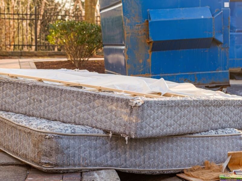 Mattresses left outside of apartment building after someone didnt know can you leave furniture in an apartment when you move out. Old mattresses are on the floor as garbage by two large blue dumpsters.