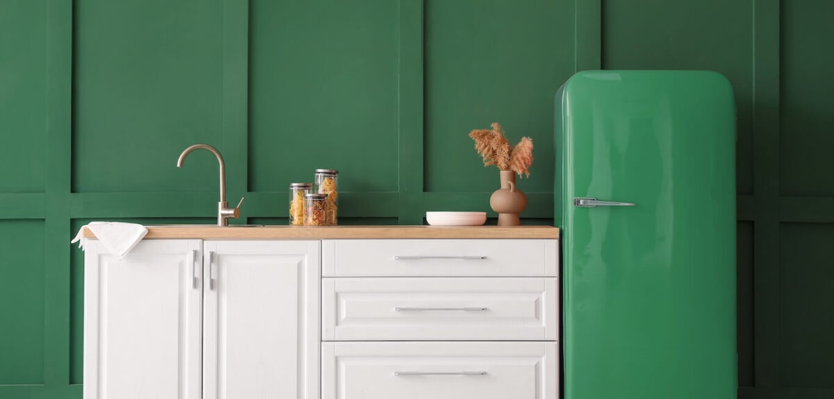 A kitchen painted dark green with white cabinets and a matching dark green refrigerator.