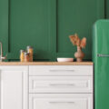 A kitchen painted dark green with white cabinets and a matching dark green refrigerator.