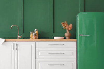 A kitchen painted dark green with white cabinets and a matching dark green refrigerator.