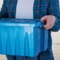 A man carries a plastic blue bin packed with belongings.