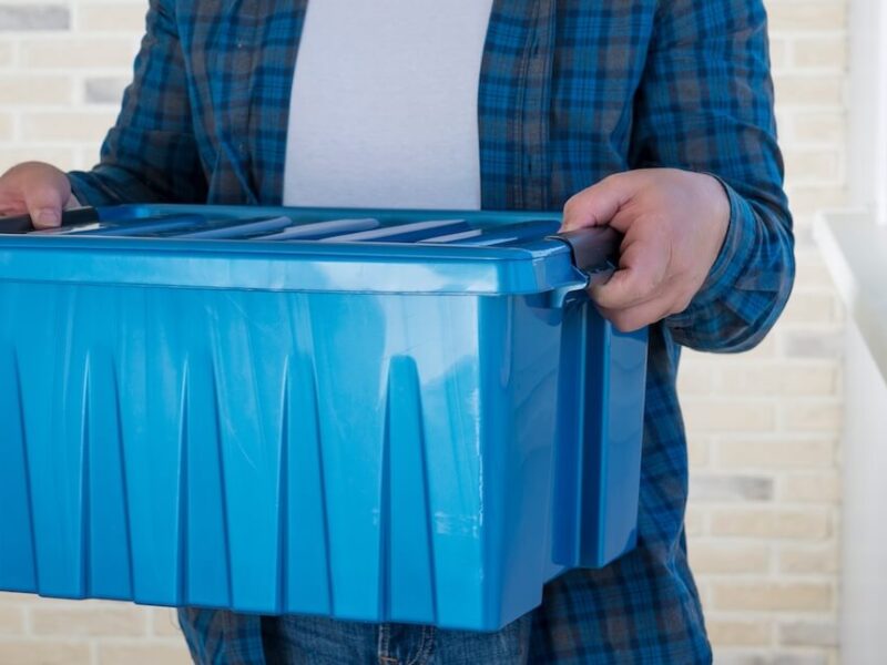 A man carries a plastic blue bin packed with belongings.