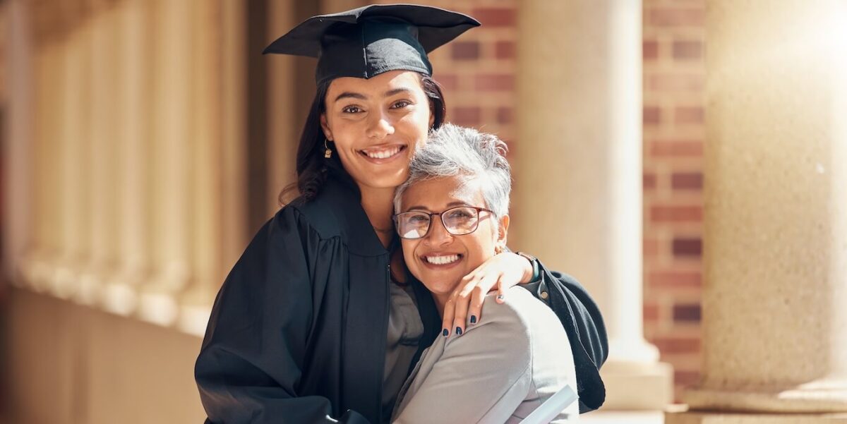 A young woman in a graduation cap and gown hugs her mom.