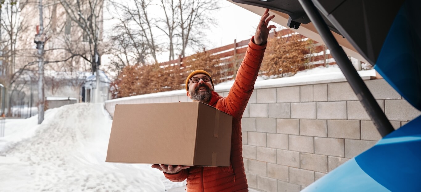 A man loading boxes into a car in the snow.