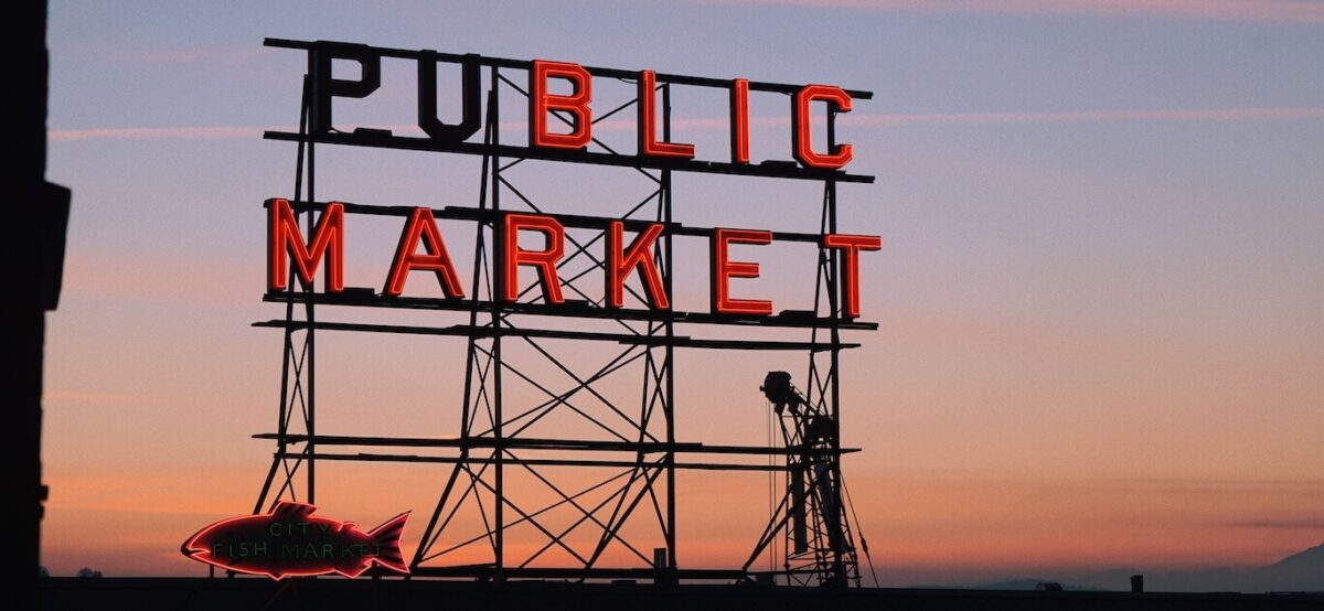 A sign for Pike Place Market in Seattle with the sunset behind it.