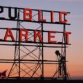 A sign for Pike Place Market in Seattle with the sunset behind it.