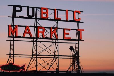 A sign for Pike Place Market in Seattle with the sunset behind it.