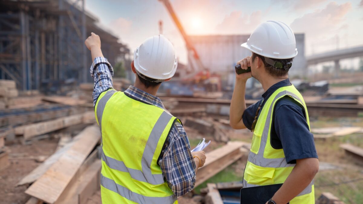 two construction project managers in safety gear discussing site progress at a busy construction site.