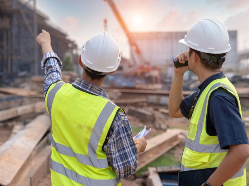 two construction project managers in safety gear discussing site progress at a busy construction site.