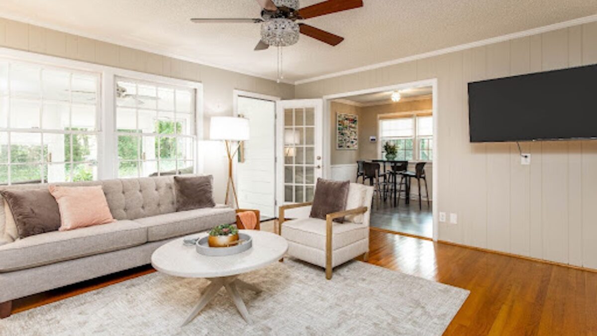 Beautifully curated rental home with furniture rental from CORT Furniture Rental, illustrating why people rent furniture and the benefits of renting furniture. Neutral decor including a couch, armchair, rug, dining set, floor lamp, modern coffee table, and flatscreen TV are visible.