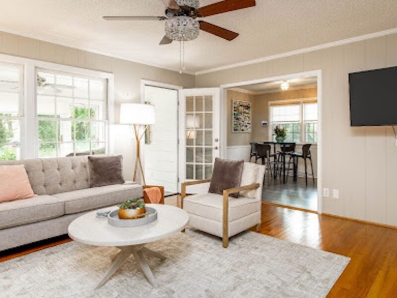 Beautifully curated rental home with furniture rental from CORT Furniture Rental, illustrating why people rent furniture and the benefits of renting furniture. Neutral decor including a couch, armchair, rug, dining set, floor lamp, modern coffee table, and flatscreen TV are visible.