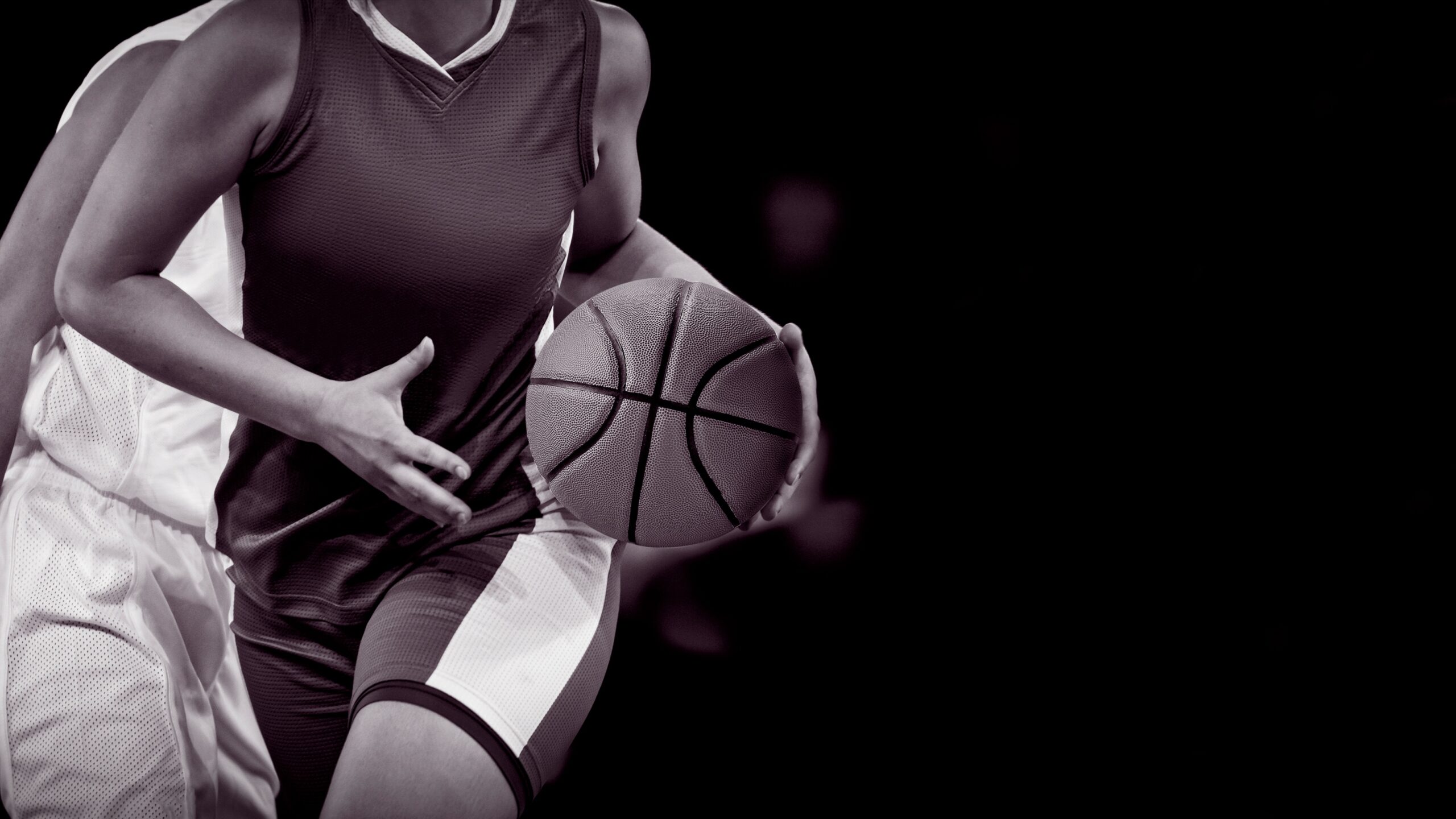 Black-and-white close-up of two basketball players in action, emphasizing intensity and competition — one grips the ball while the other defends.